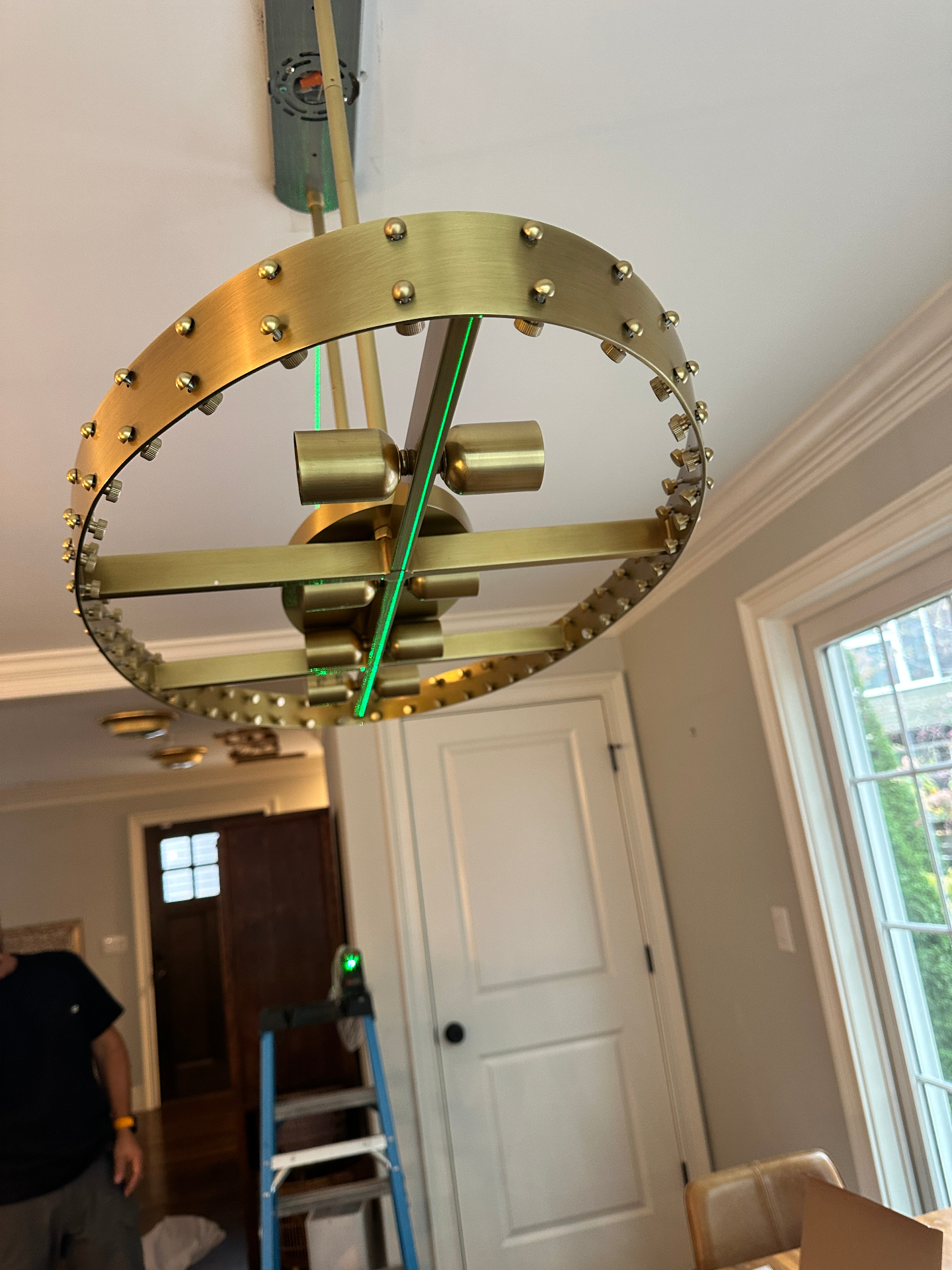 Brass ring chandelier installation in progress with laser alignment