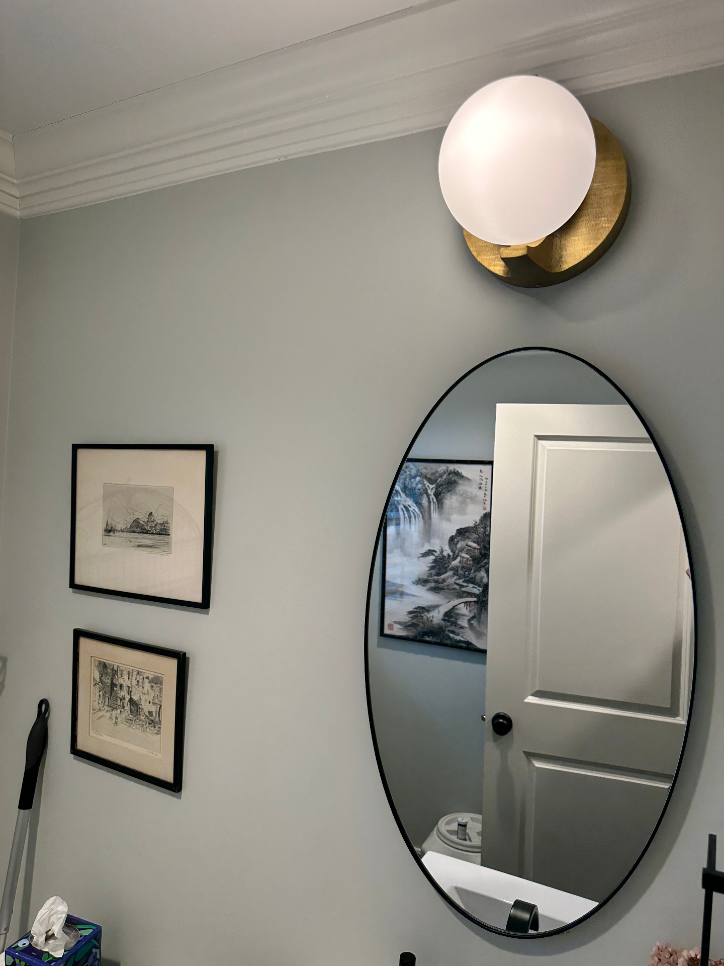Modern brass globe sconce above oval mirror in bathroom